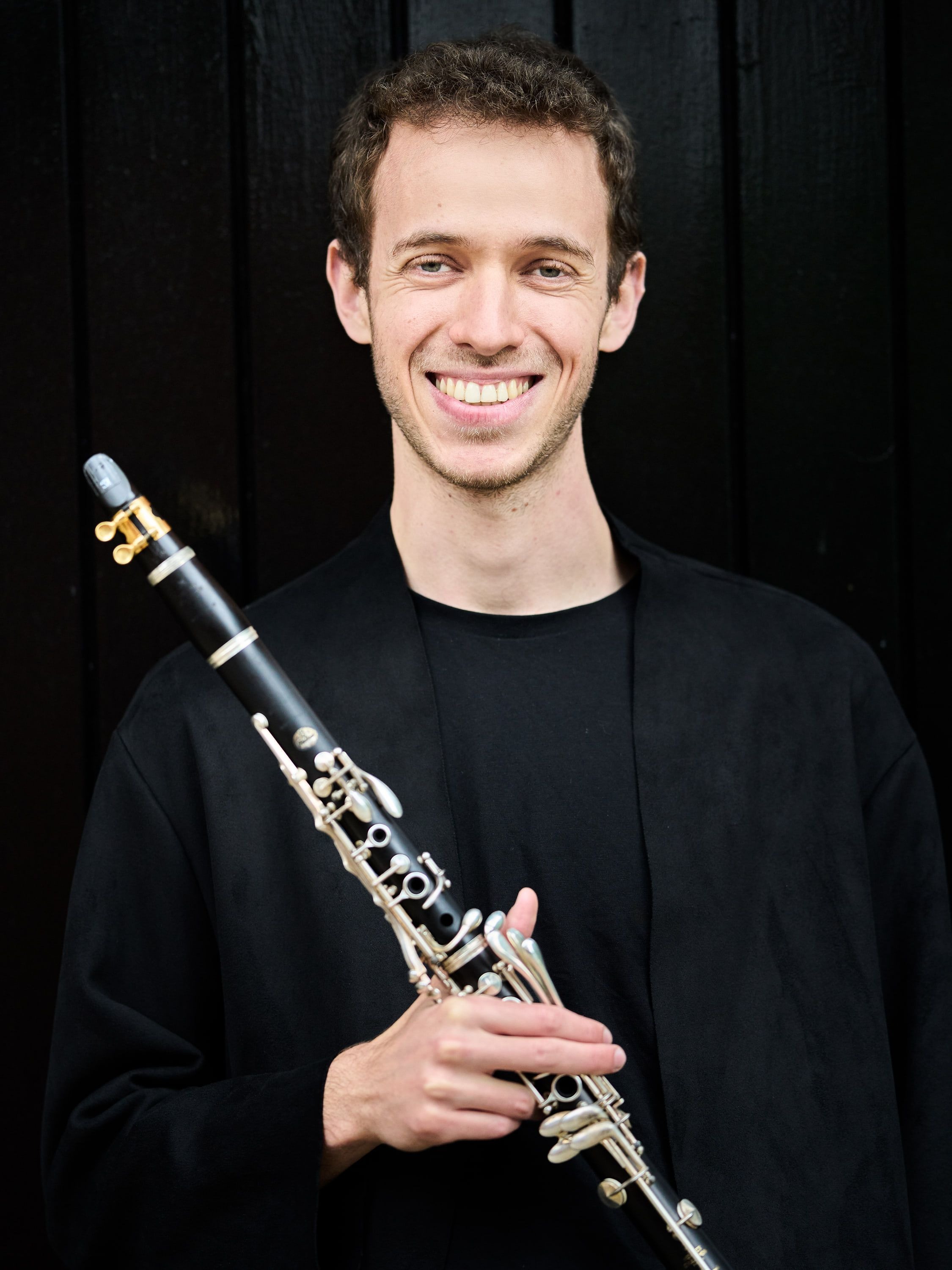 Jonathan Leibovitz smiling against a dark wall, clarinet across his chest