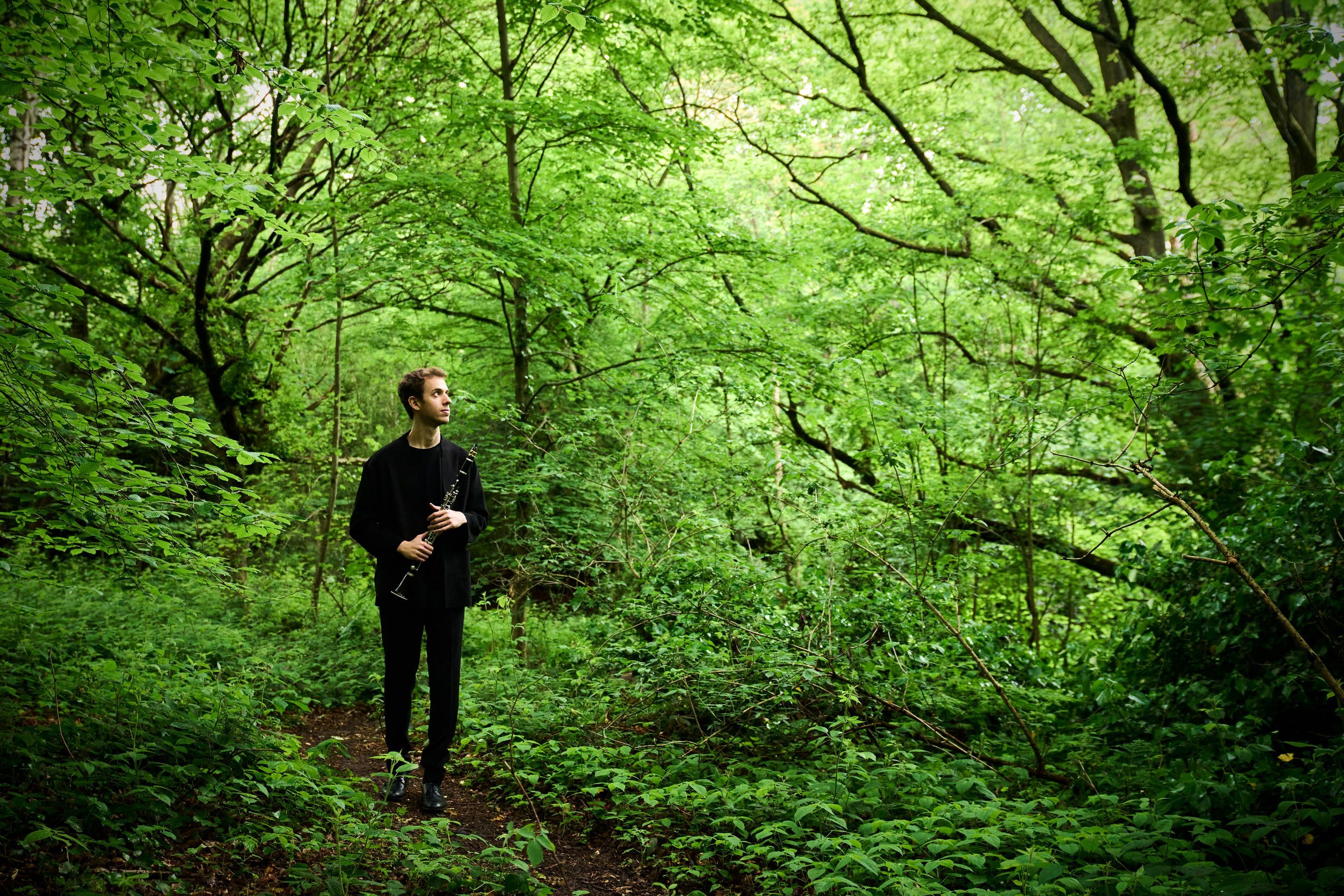 Jonathan Leibovitz walking through green woodland with his clarinet