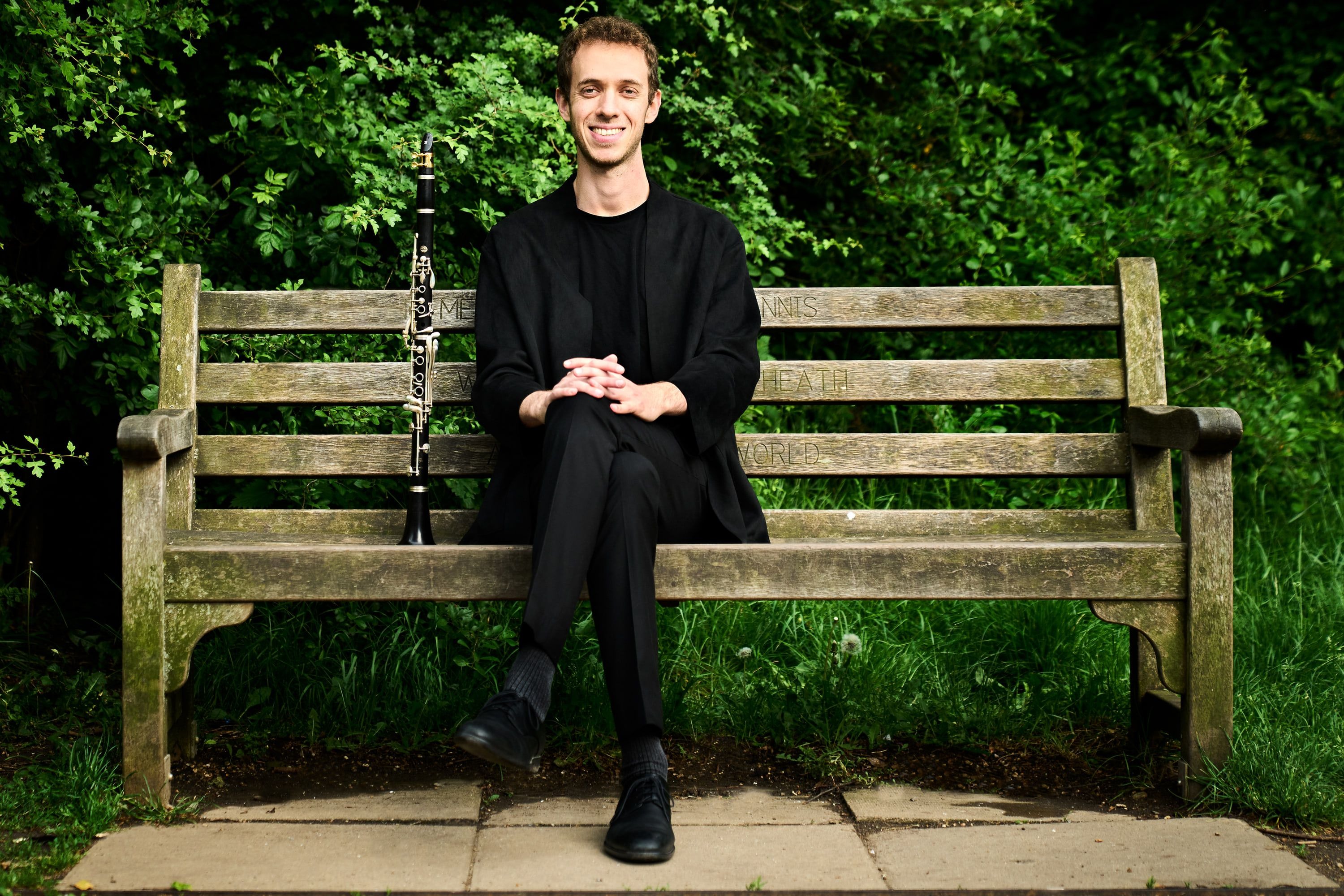 Jonathan Leibovitz seated on a wooden park bench, his clarinet resting beside him